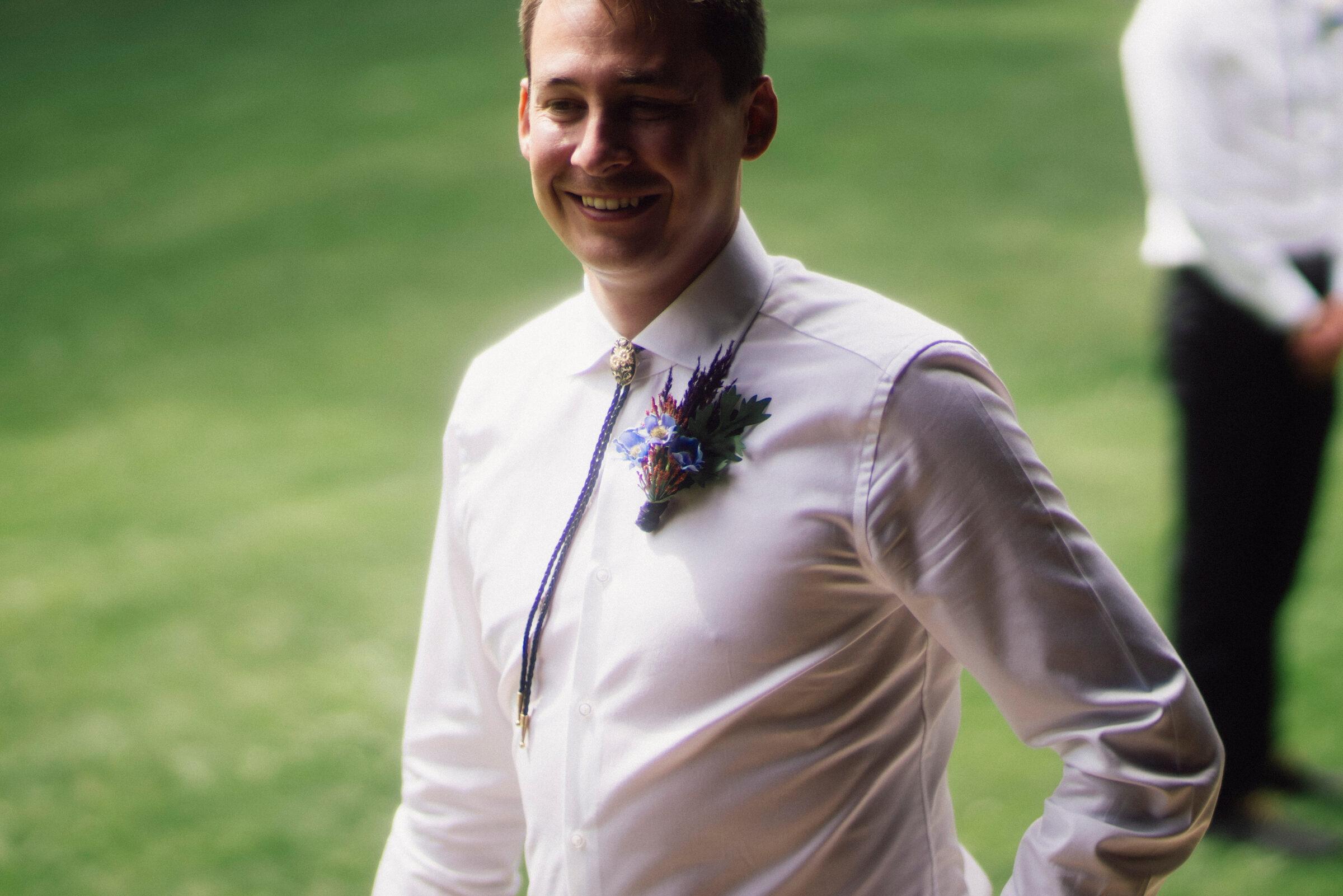 Groomsman in a bolo tie with a protea and delphinium boutonniere