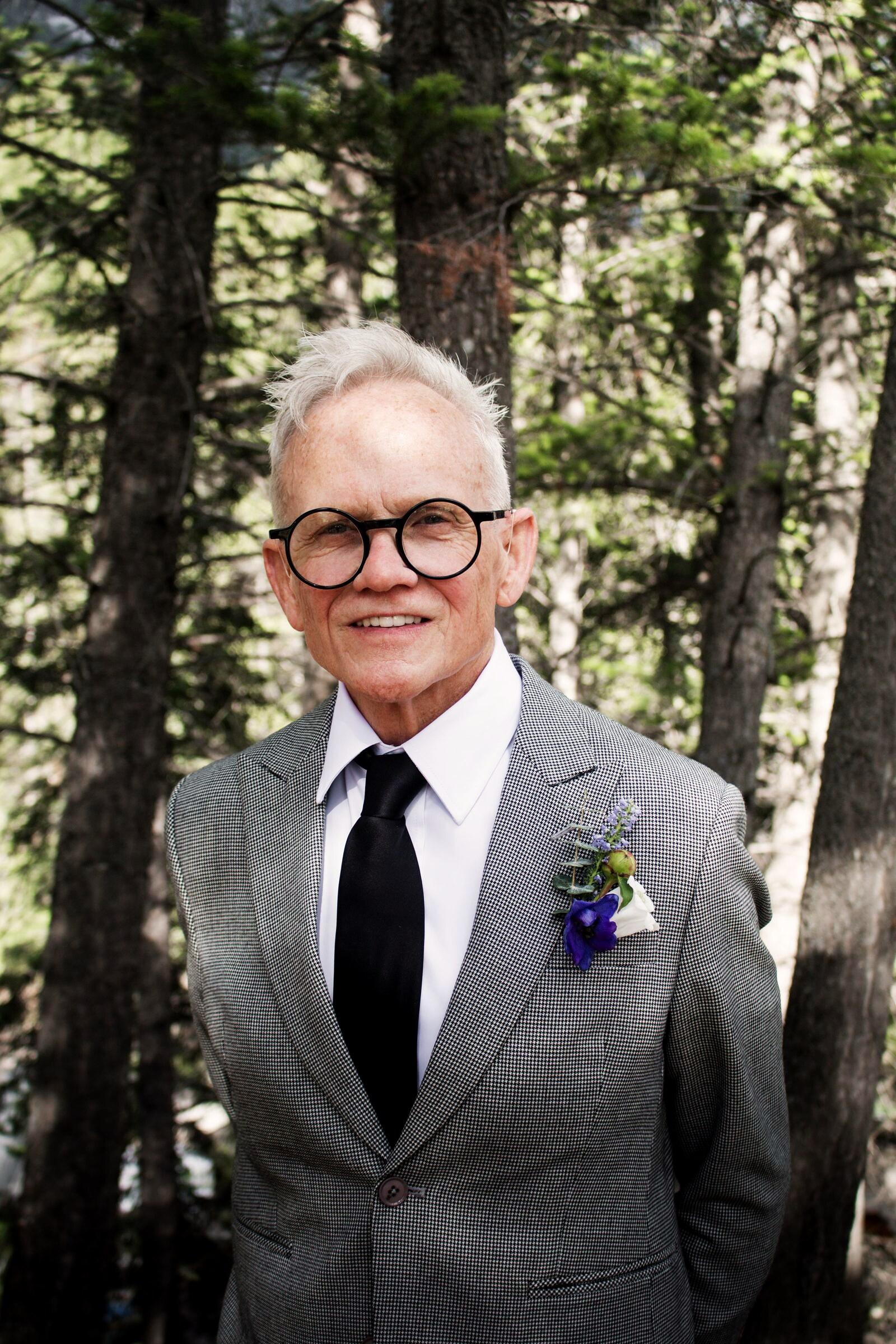 Guest in a grey suit with a thistle boutonniere among the pines