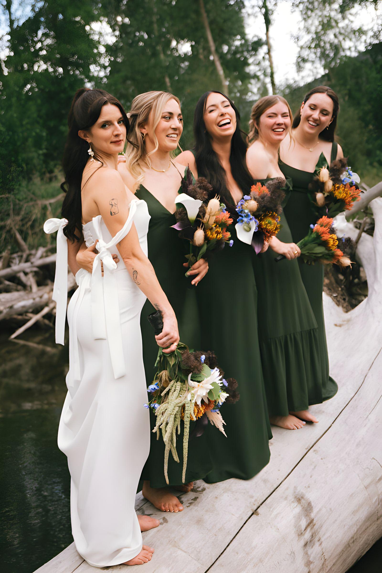 Bride and bridesmaids standing barefoot along a driftwood log above the river