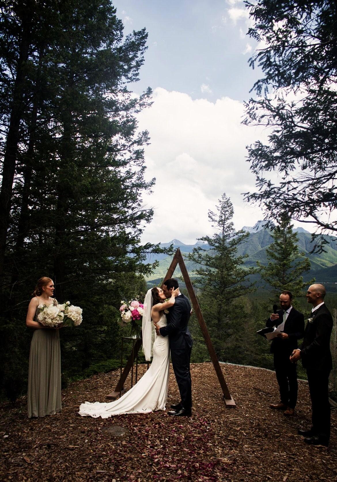 Ceremony at the A-frame arch with mountains beyond the trees