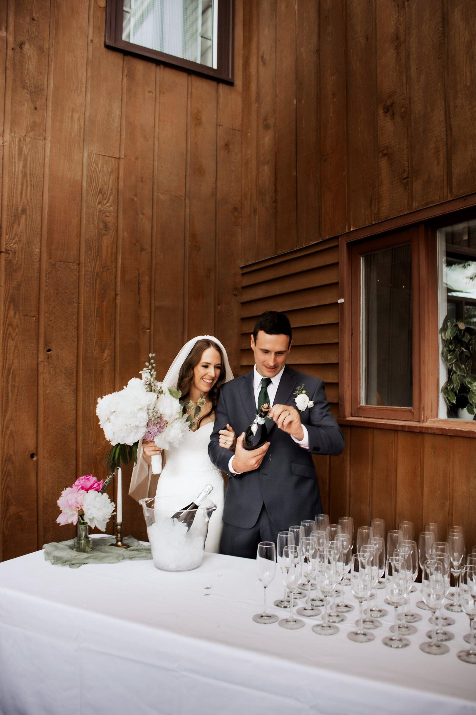 Couple opening champagne beside a bud vase of peonies
