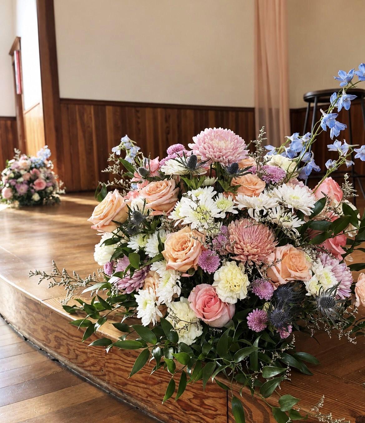 Pastel arrangement of roses, dahlias, and delphinium on a hall stage