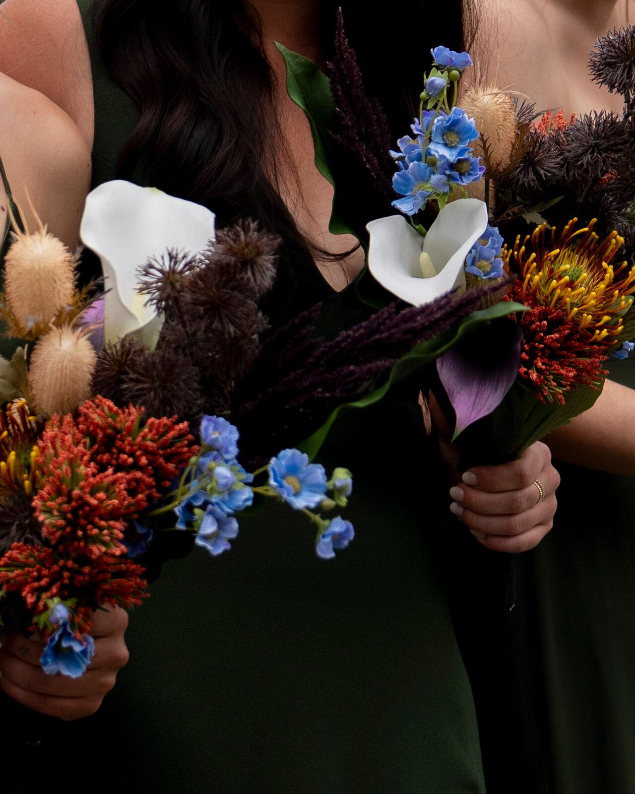 Close detail of pincushion protea, calla lilies, dried thistle, and blue delphinium