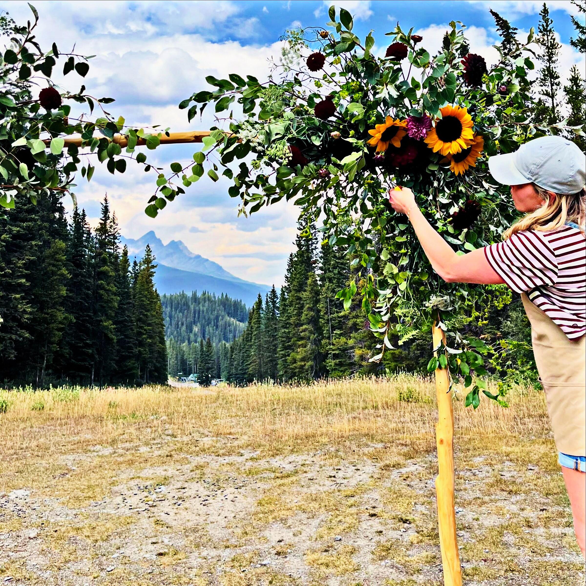 Toni installing a floral ceremony arch with the Rockies behind